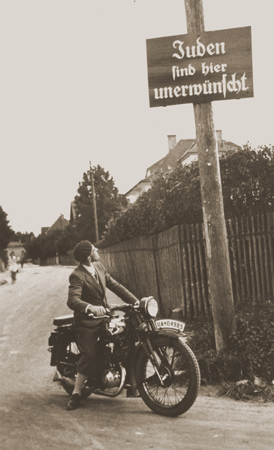 A motorcyclist reads a sign stating "Jews are not welcomed here." Germany, ca. 1935. — US Holocaust Memorial Museum, courtesy of Margaret Chelnick